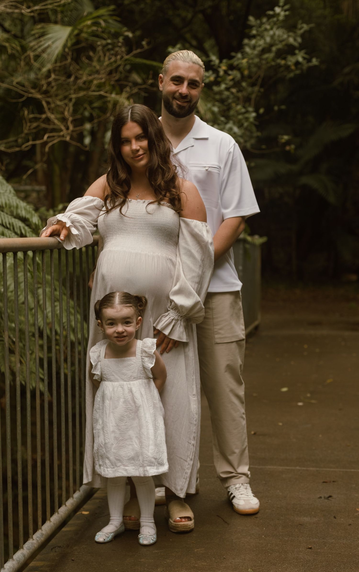 Pregnant mum and her partner standing with their young daughter on a rainforest walkway during a family maternity photography session.