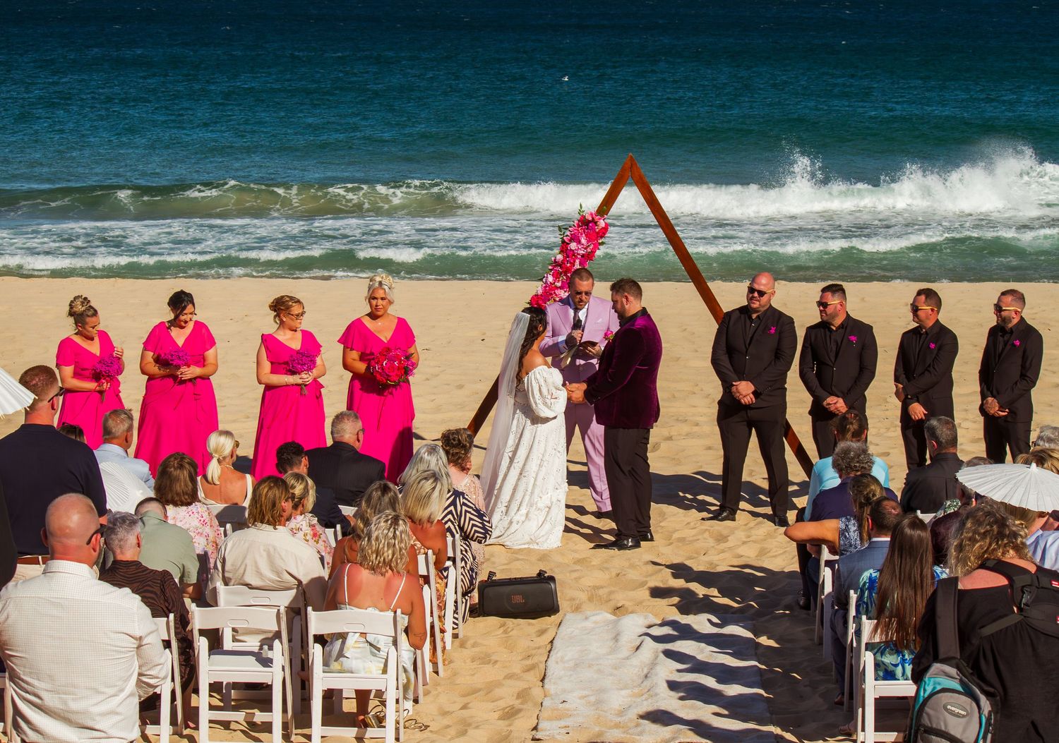 Wide shot of the beach wedding ceremony with guests watching the bride and groom exchange vows.