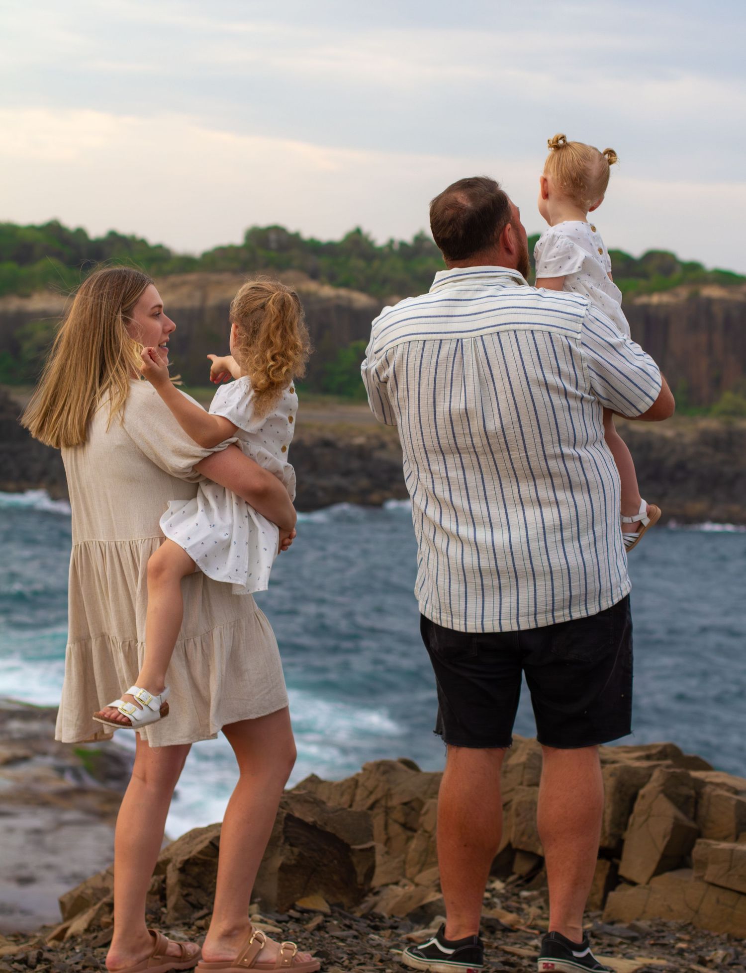 Family photographed from behind overlooking the ocean at Bombo Quarry, capturing a relaxed sunset family photoshoot.
