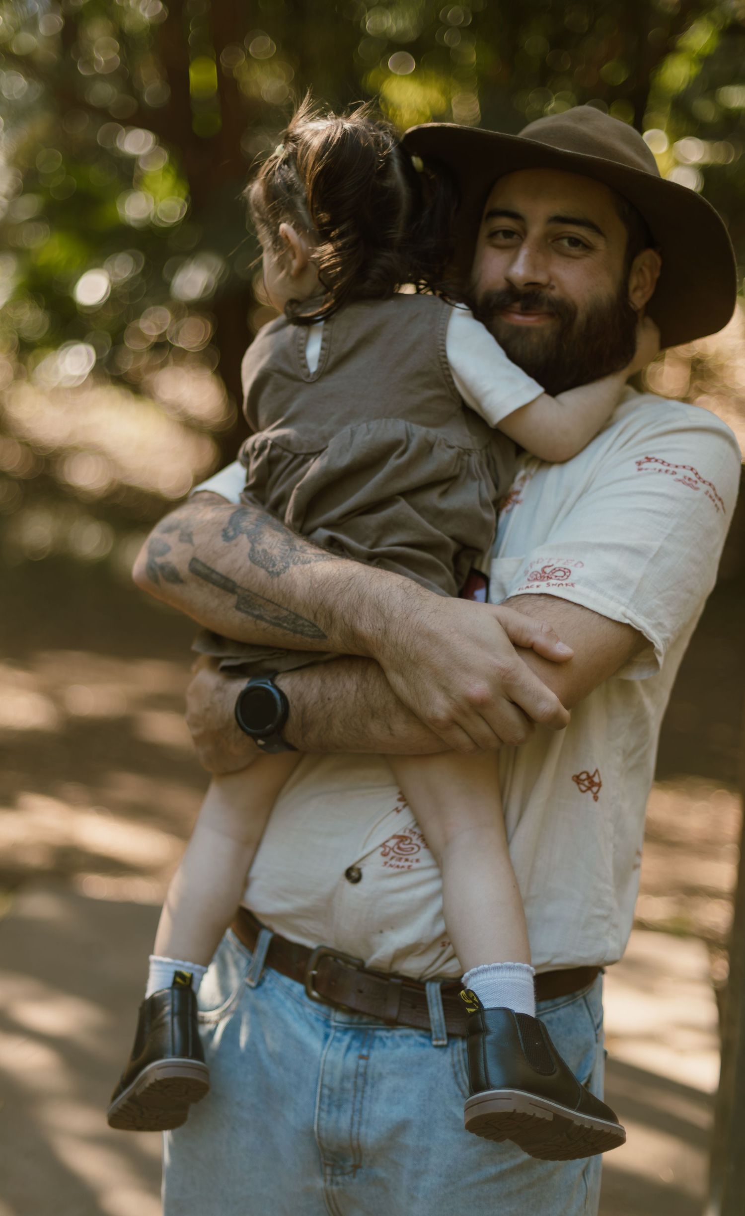 Dad cuddling his young daughter close during an outdoor family photography session surrounded by greenery.