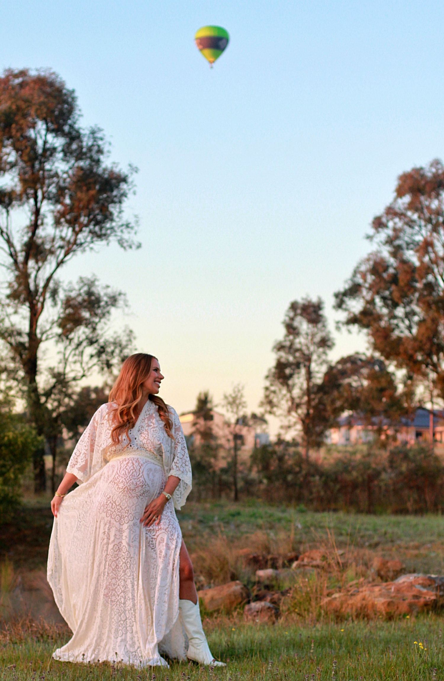 Expectant mother twirling her dress in soft sunrise light.