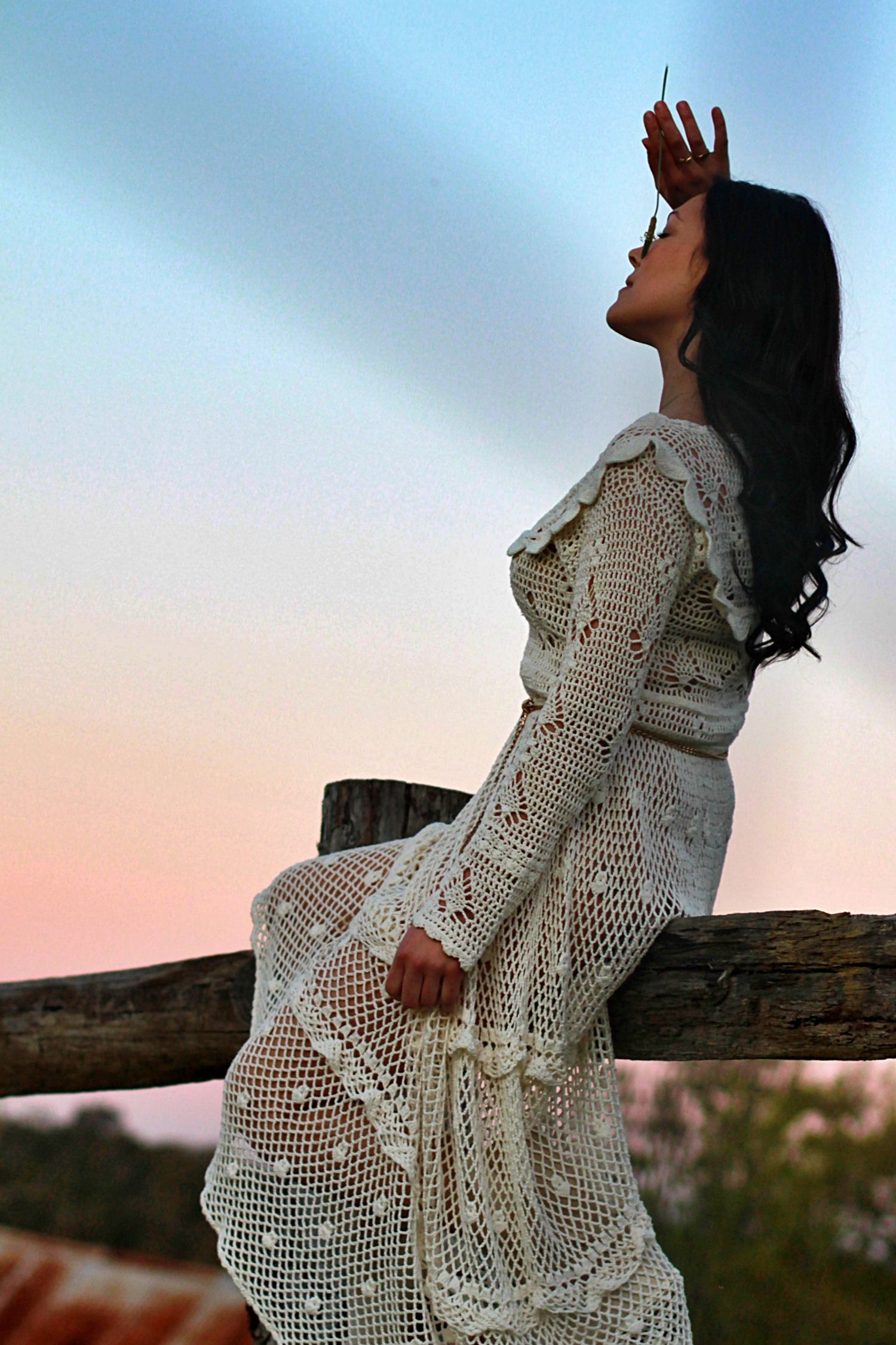 Woman sitting on a fence surrounded by nature in a rural setting