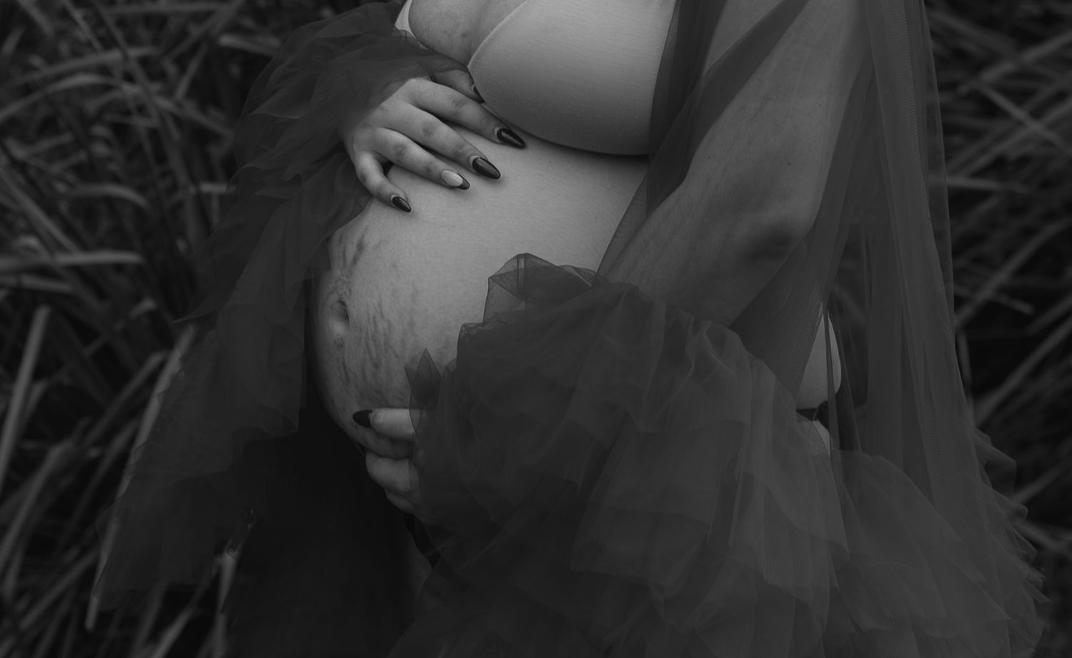 Black and white portrait of a mother gently holding her baby bump, capturing a tender and intimate moment of pregnancy.