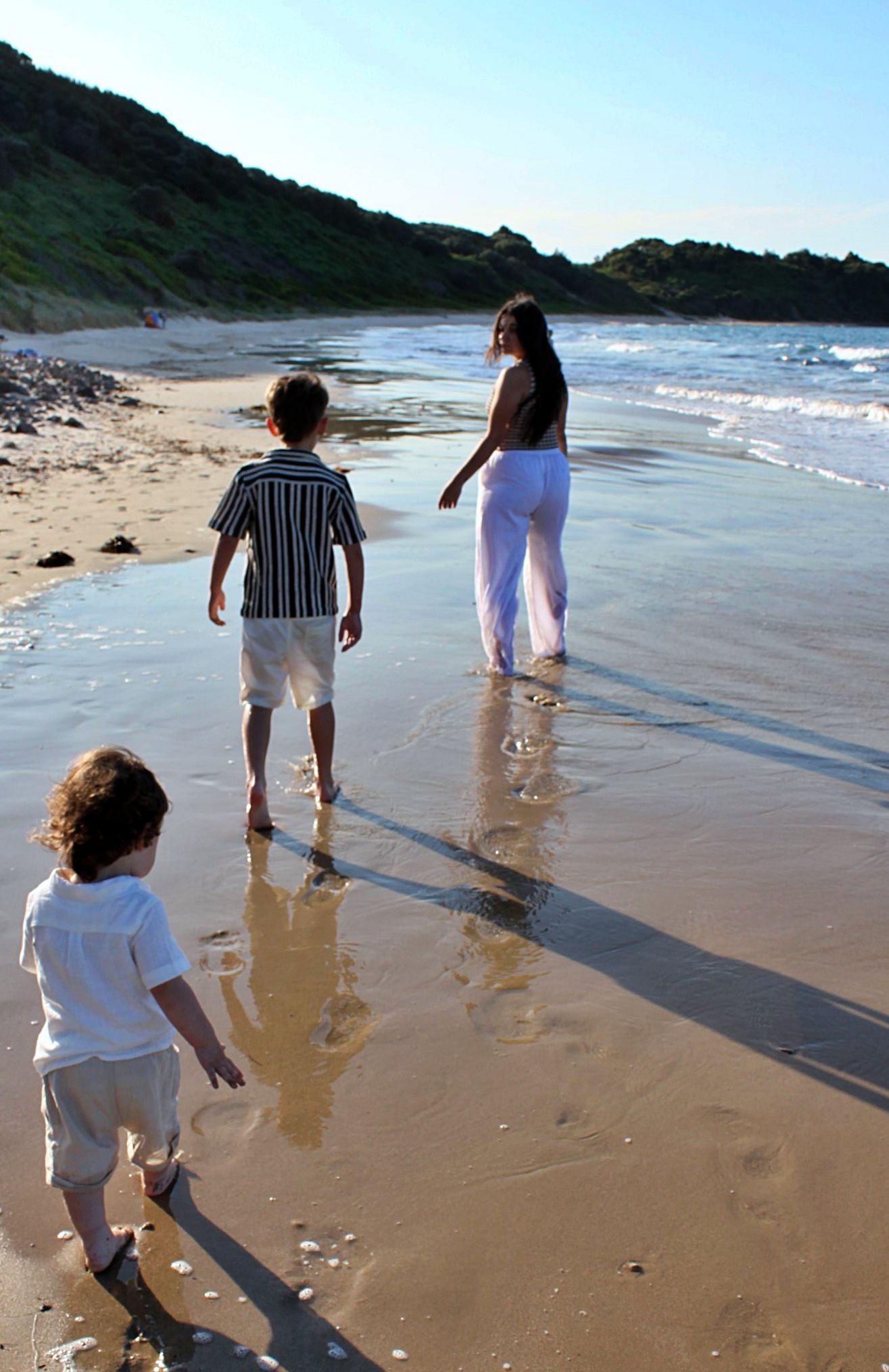 Mum running along the beach with her two children chasing her capturing a candid playful moment during a motherhood session.