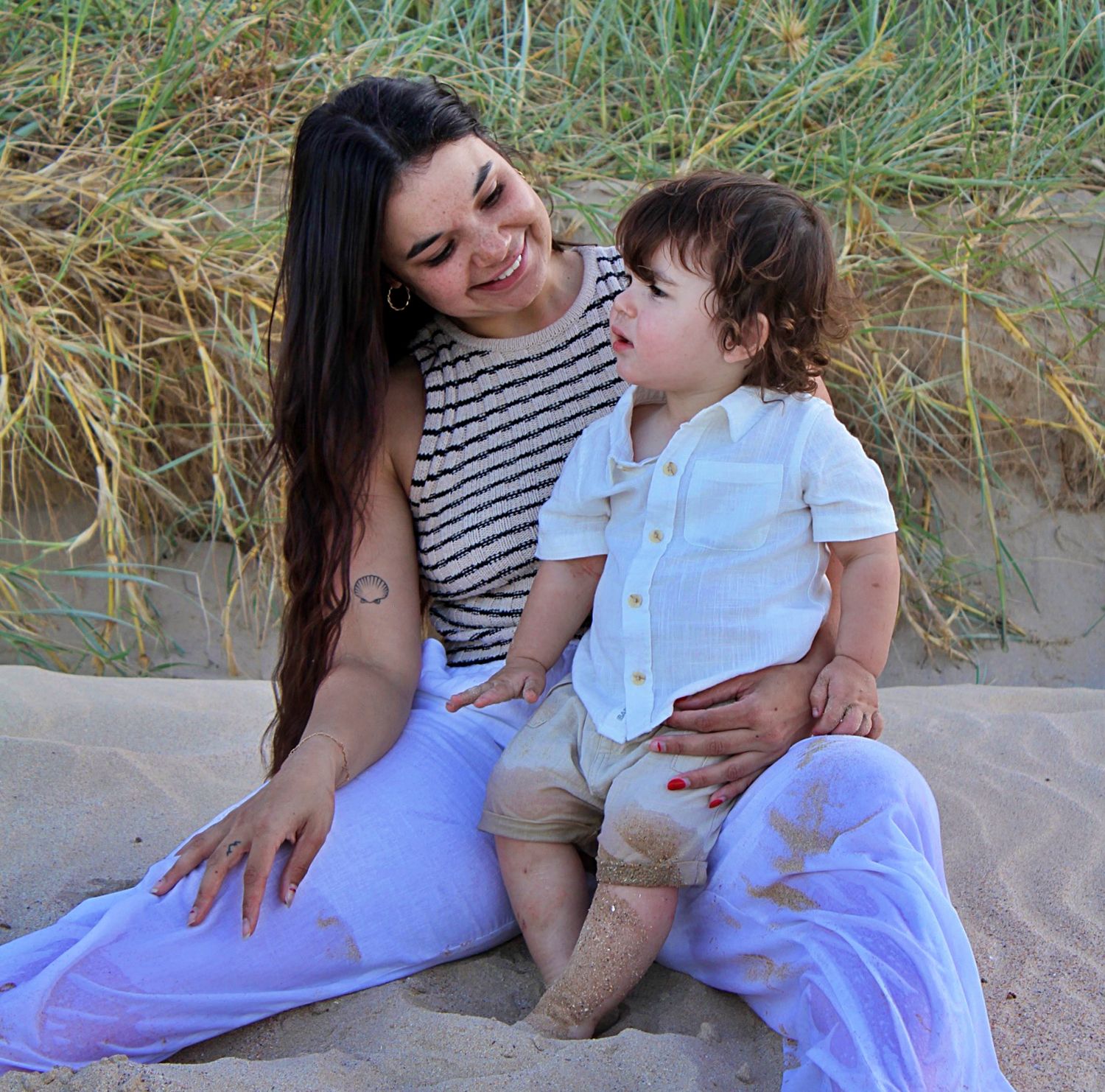 Mother and son looking at each other full of love while sitting on the beach during a motherhood session.