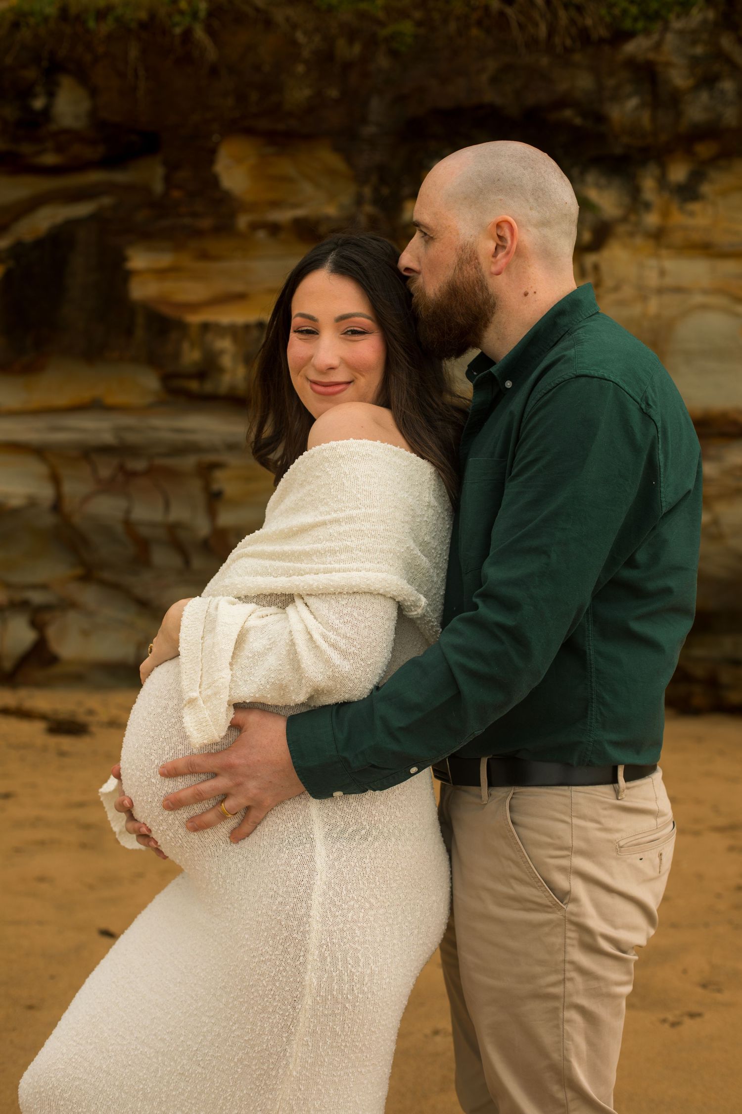 Pregnant woman standing with her partner on the beach during a relaxed maternity photography session.