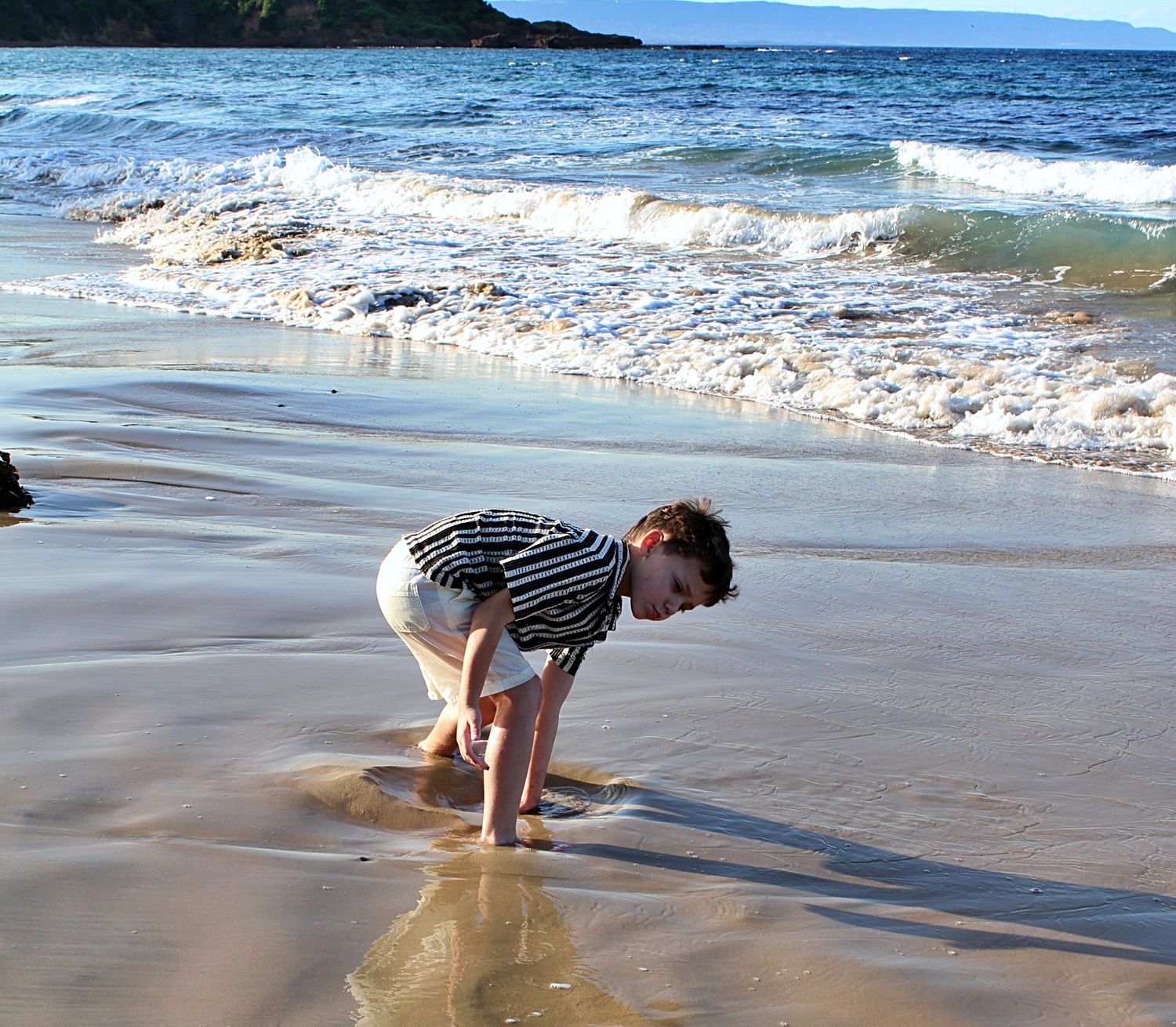 Solo candid portrait of young boy playing in the sand by the shoreline during motherhood session.