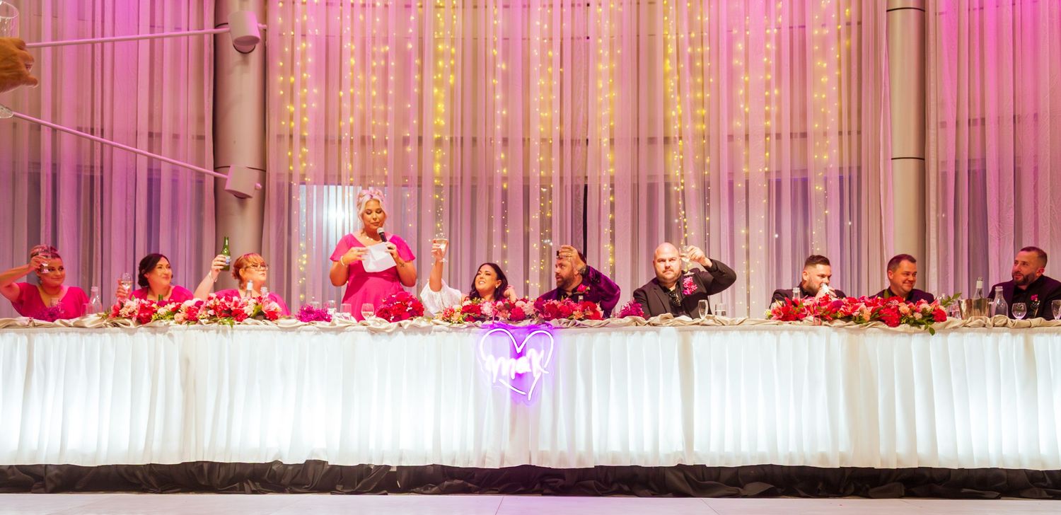 Wide shot of the bridal party seated together at the reception table celebrating the wedding.