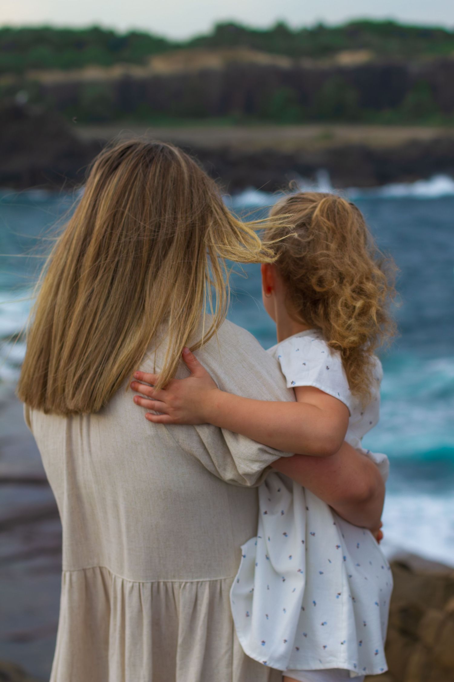 Mum holding her young daughter while they look out over the ocean during a coastal family photography session.