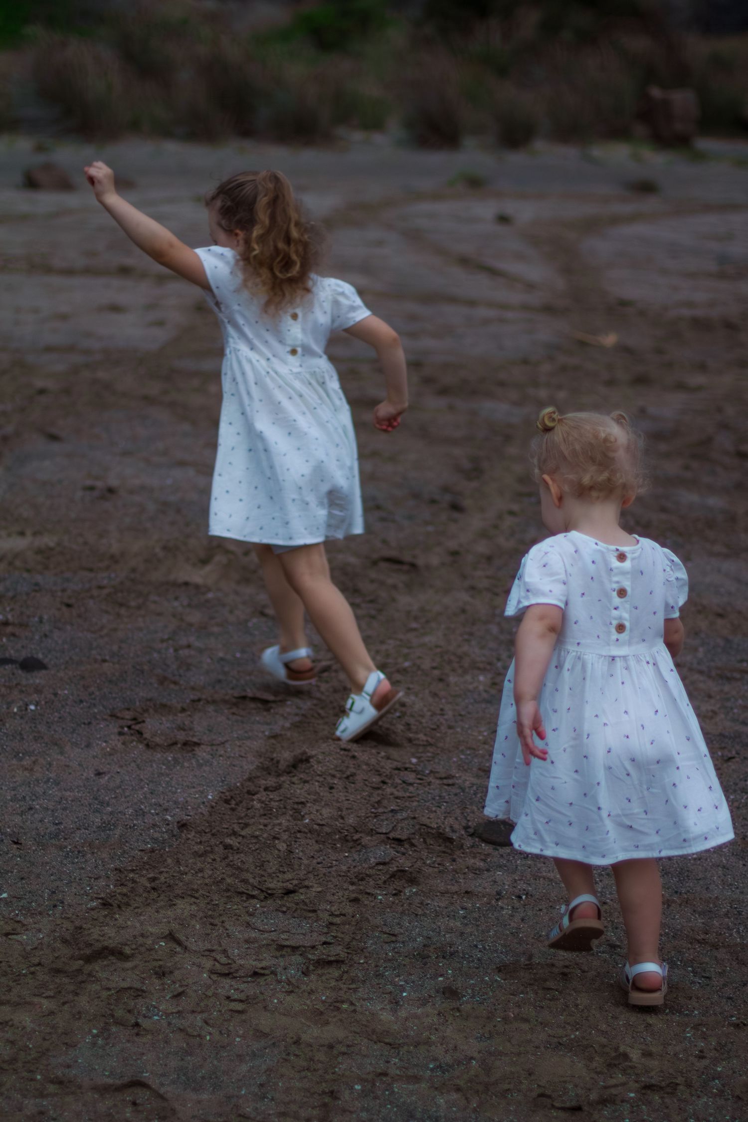Two young girls running and playing outdoors, captured from behind by an Illawarra family photographer.