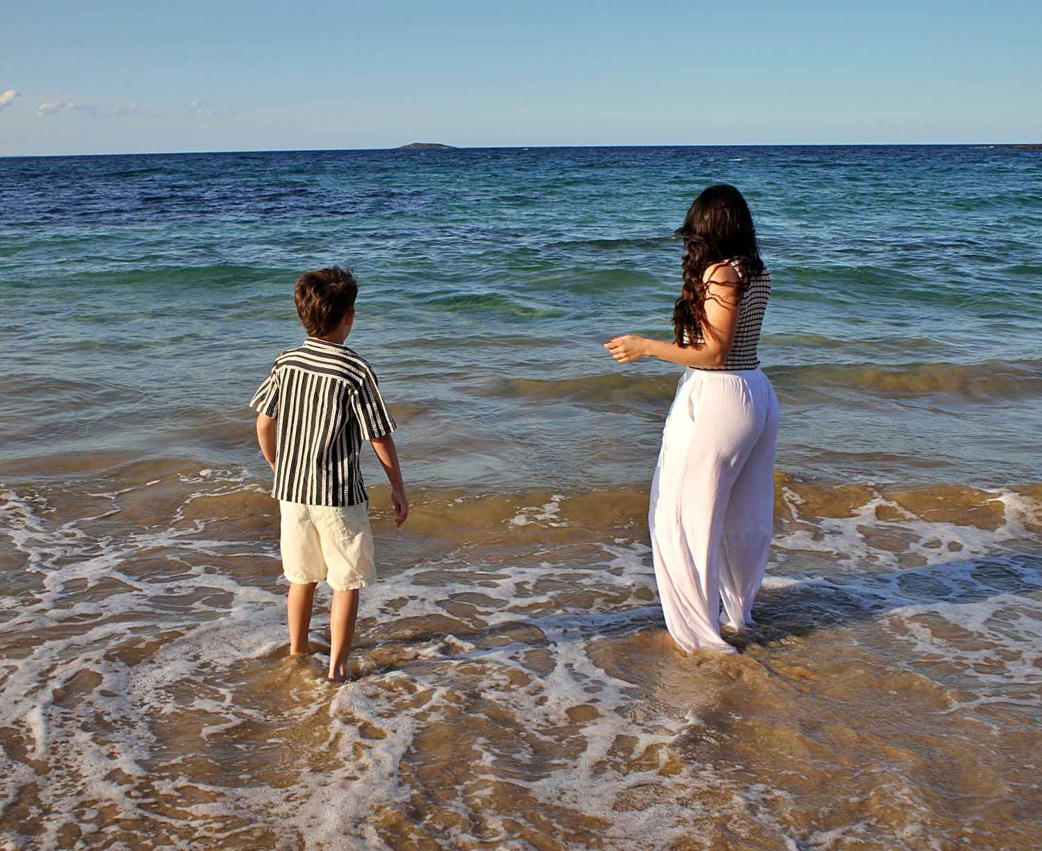 Mother and son sharing a playful moment in the water, captured from behind during a candid beach session.