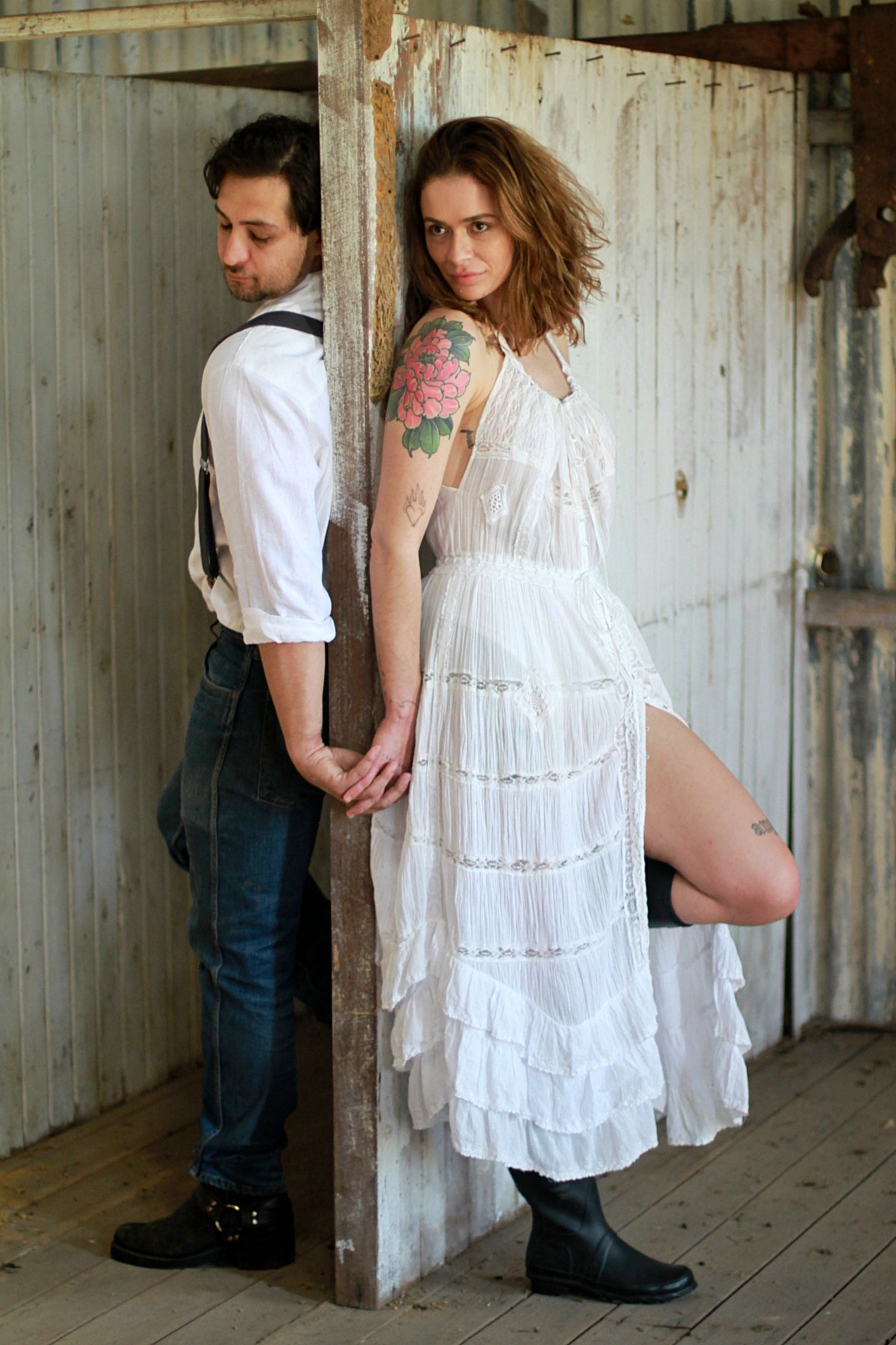 Romantic couple back-to-back in a rustic barn, capturing intimate connection and timeless love in a warm, natural setting.