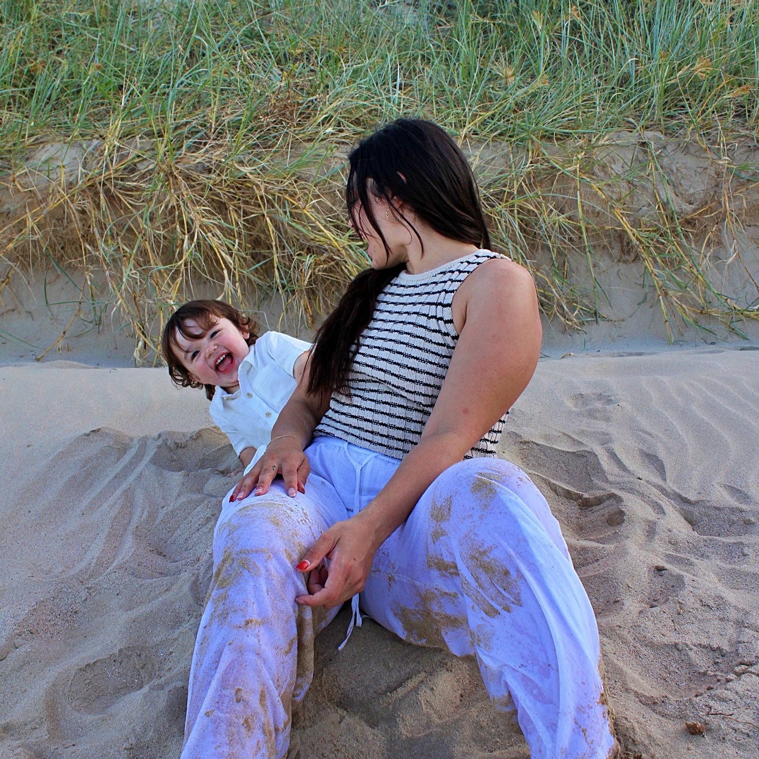 Candid motherhood session capturing a mother holding her son close while kissing his cheek by the ocean