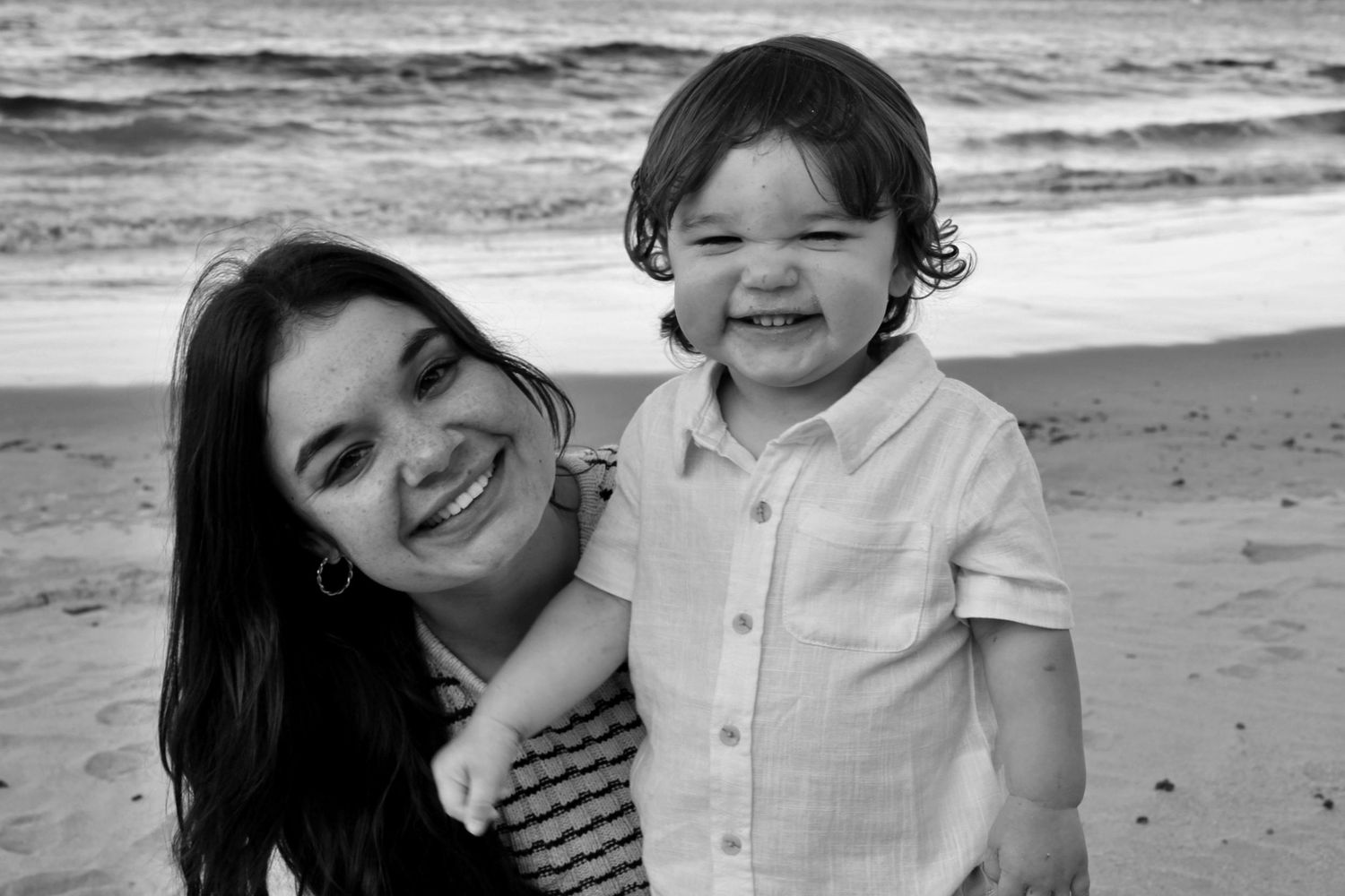 Mother and her young son smiling at the camera, sharing the same joyful smile during a beach motherhood session.