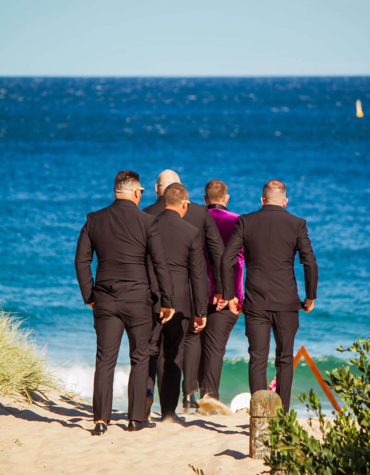 Groom and groomsmen walking along the beach toward the ceremony, candid pre-ceremony moment before the wedding begins.