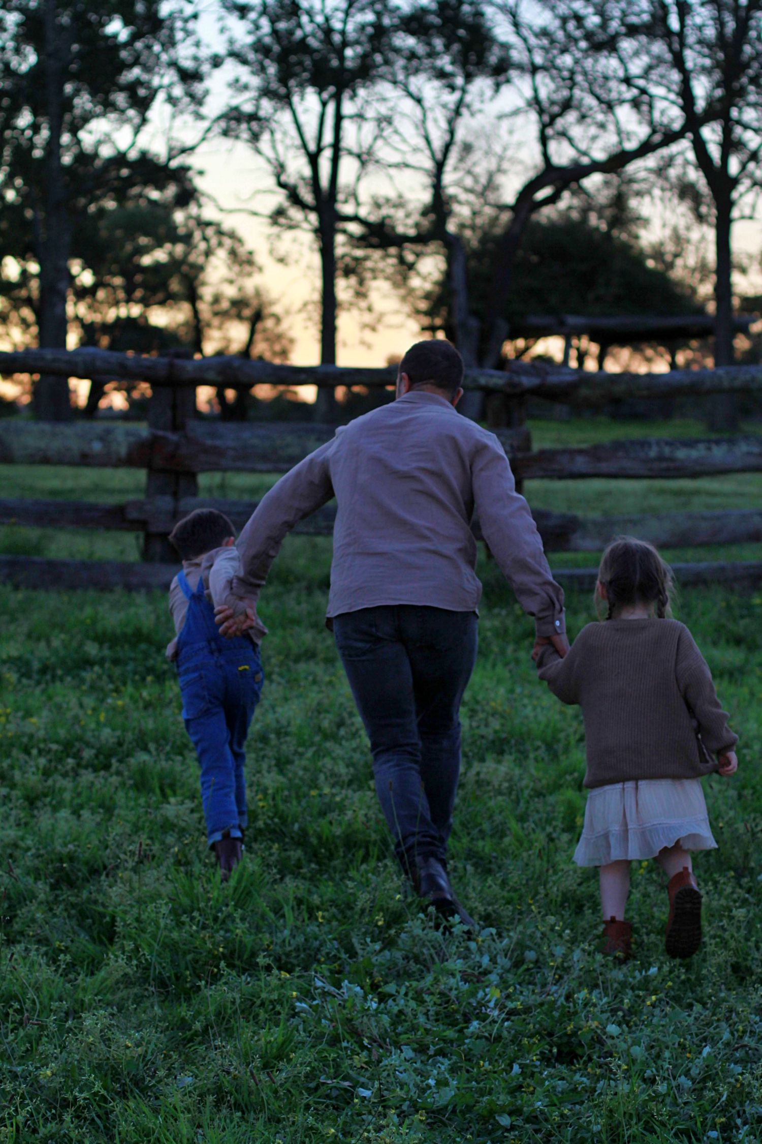 Adult holding both kids hand walking through the country fields during a family session
