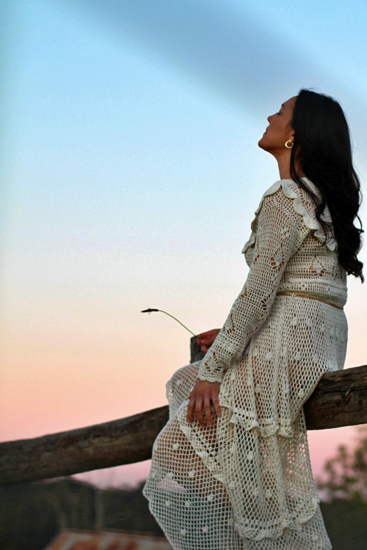 Woman sitting on a fence surrounded by nature in a rural setting