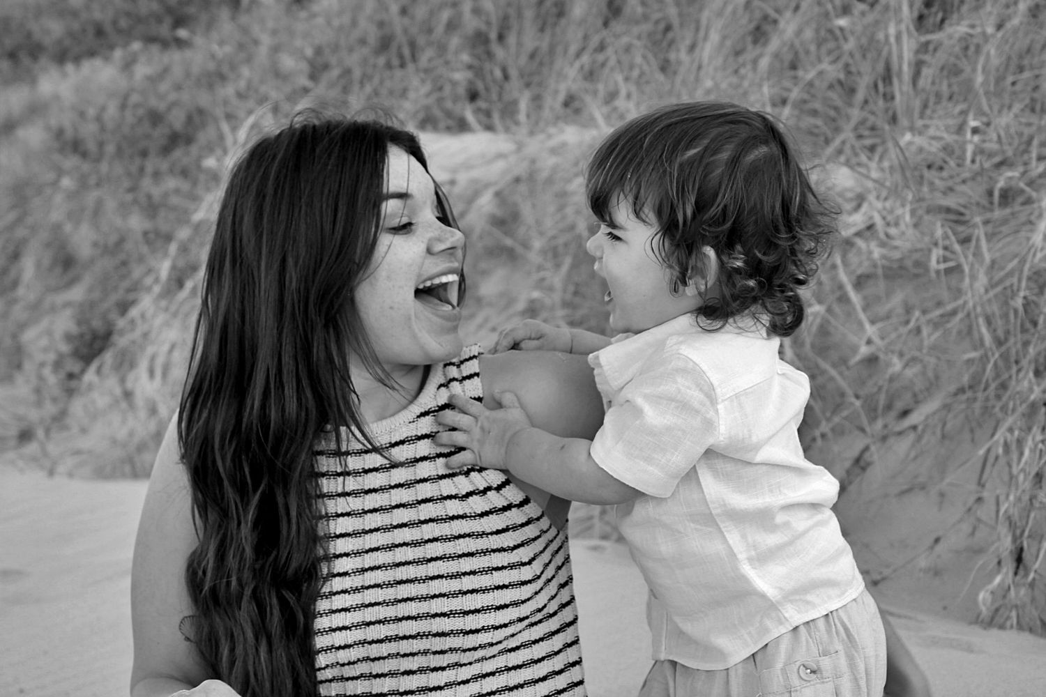 Mother smiling at her son while he looks at her during a beach motherhood session on the sand.