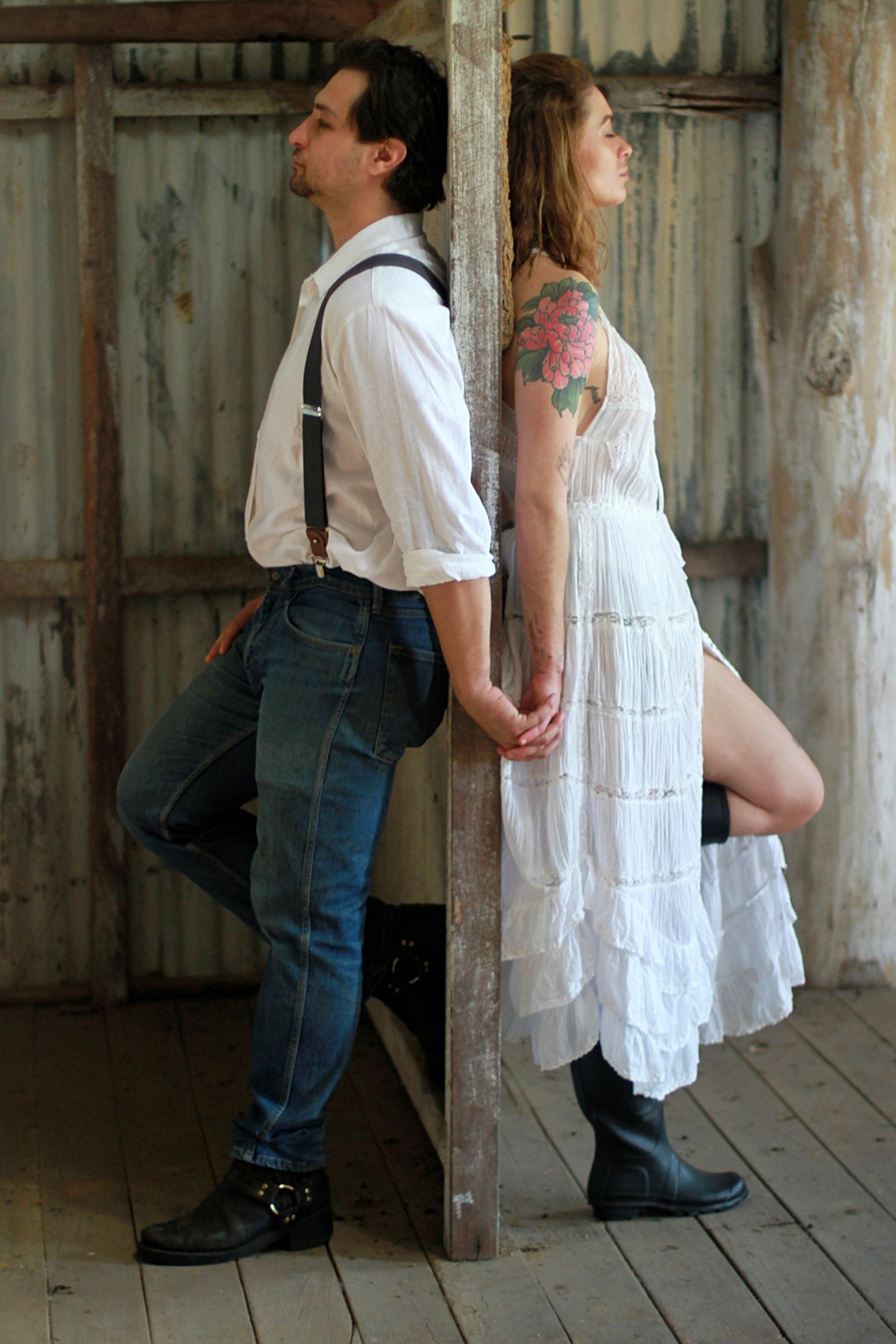 Couple leaning back-to-back against a rustic barn wall and holding hands, captured in a romantic lifestyle photoshoot.