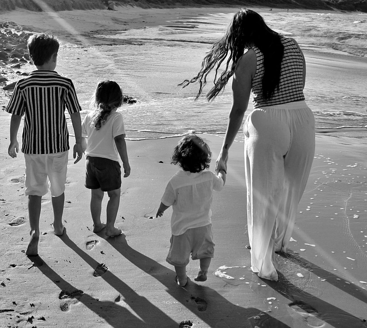 Mother spending time with her three young sons during a relaxed beach motherhood photography session, capturing natural family connection.