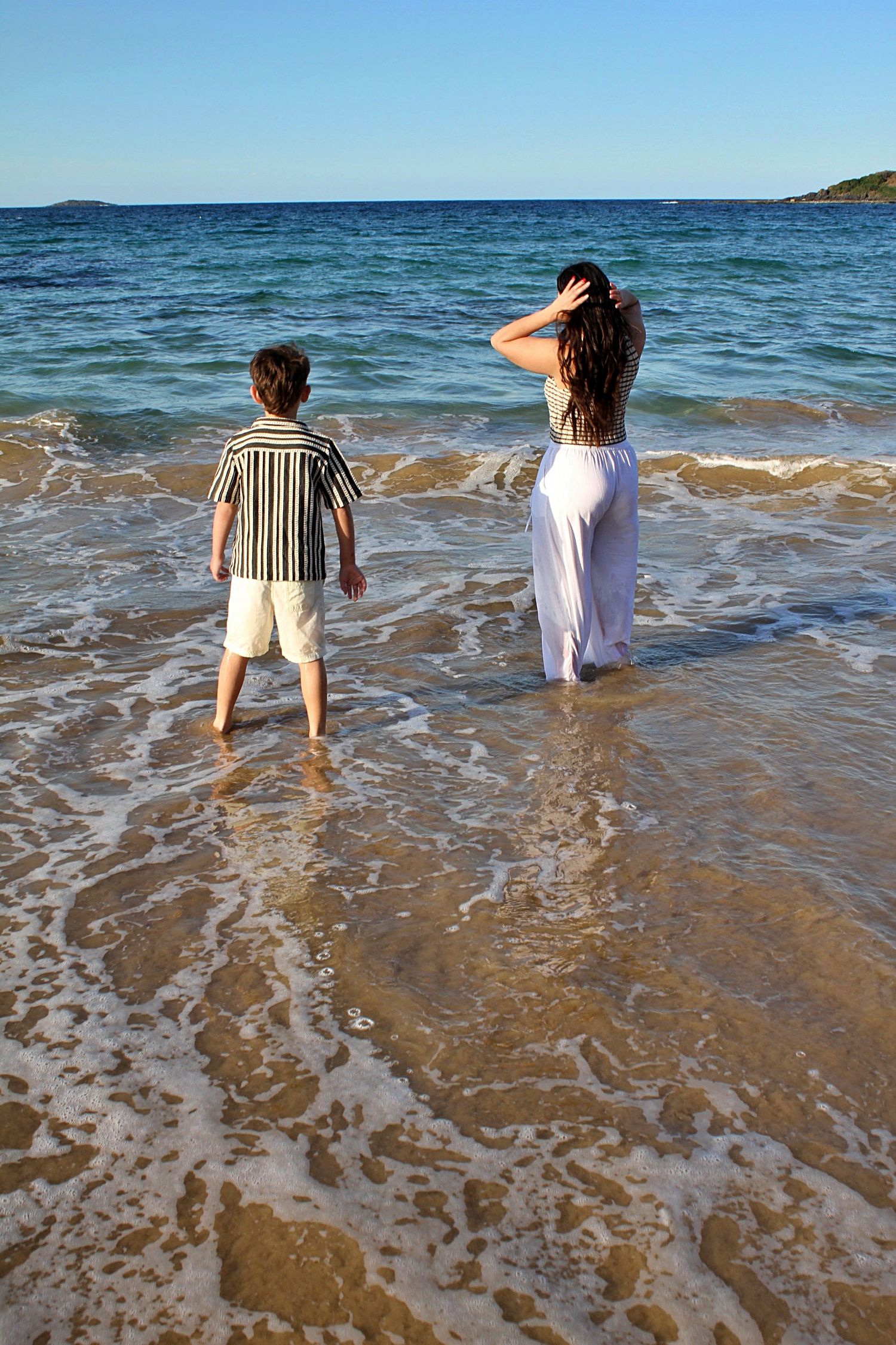 Mother and son sharing a quiet moment in the water, captured from behind during a candid beach session.