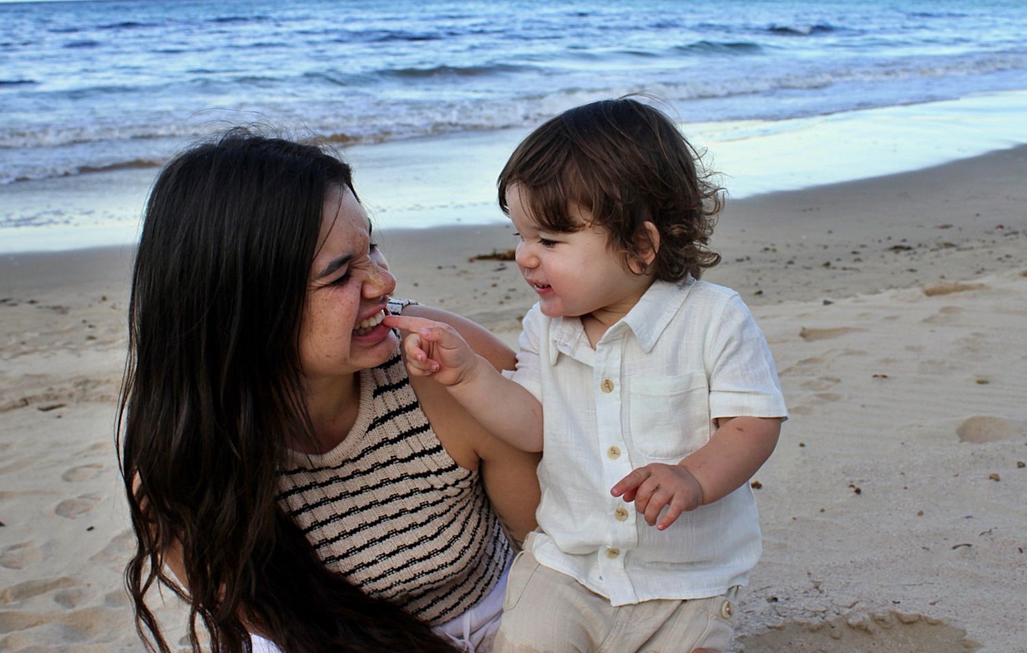 Candid moment of a mum laughing and playing with her youngest son on the beach.