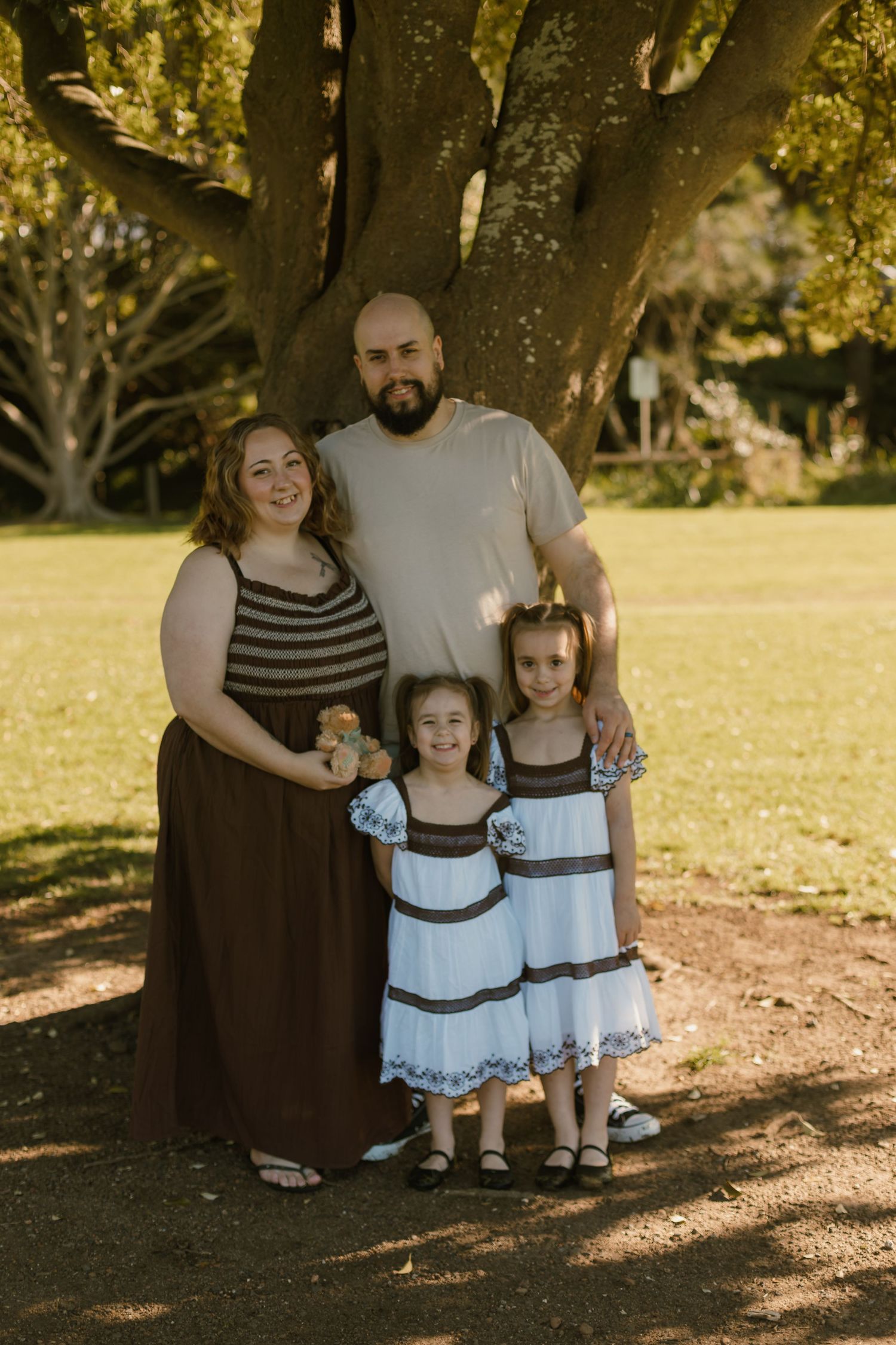 Mum and Dad standing with their two daughters beneath a large tree during an outdoor family photography session.