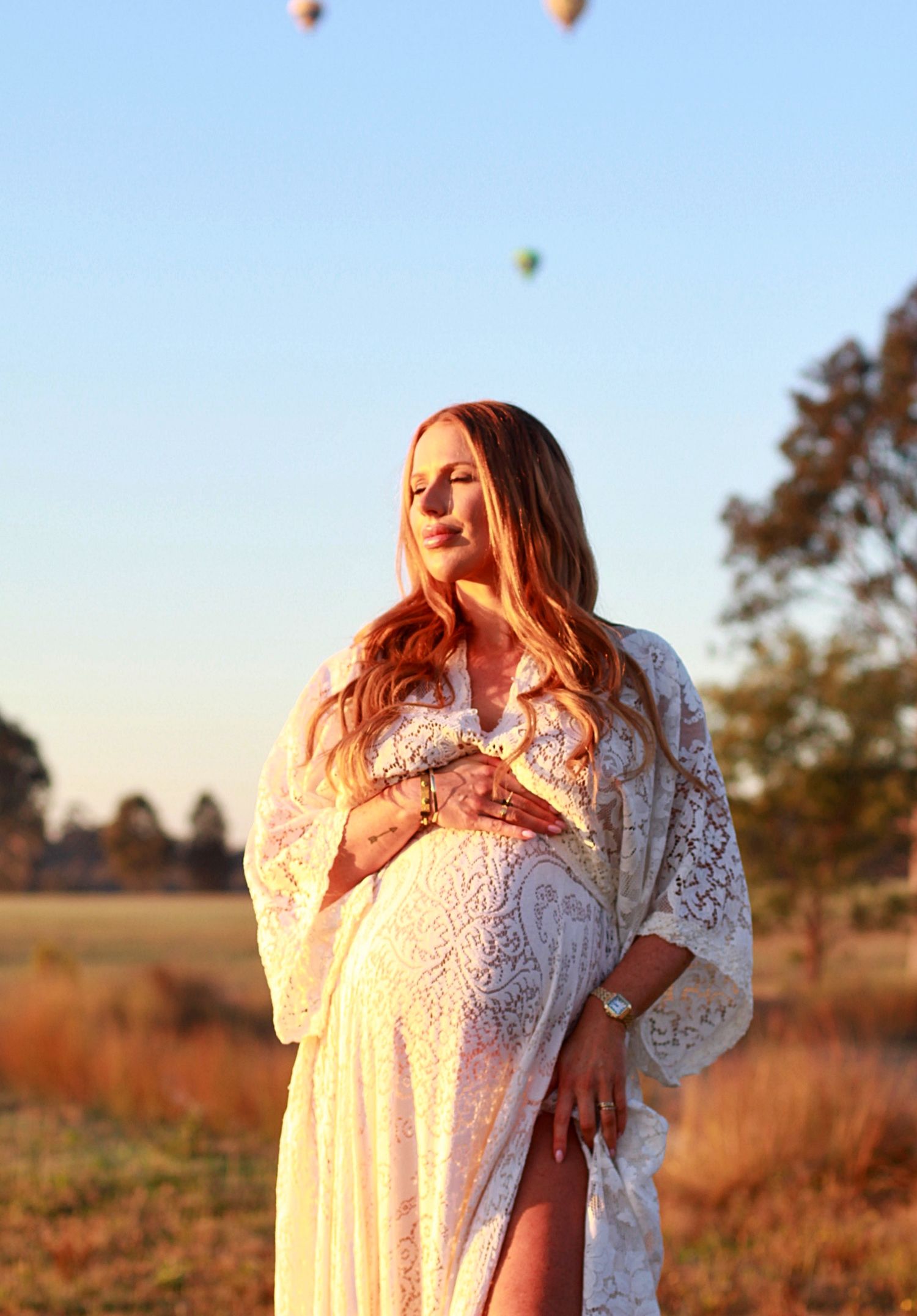 Mumma to be holding her bump, with hot air balloons rising in the background with A Lasting Impression Photography.
