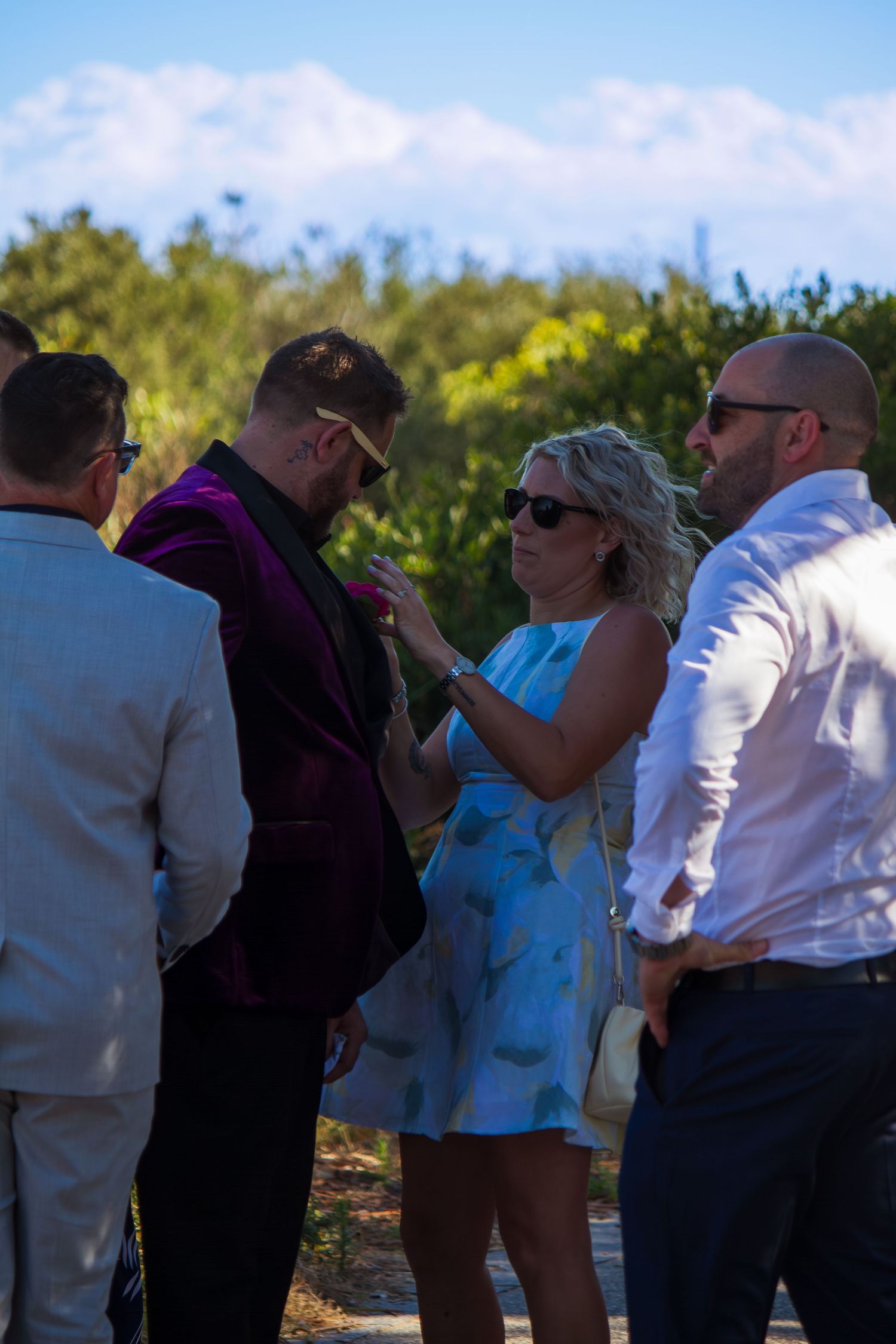 Family helping the groom adjust his tux before the ceremony, candid wedding preparation moment before walking down the aisle.