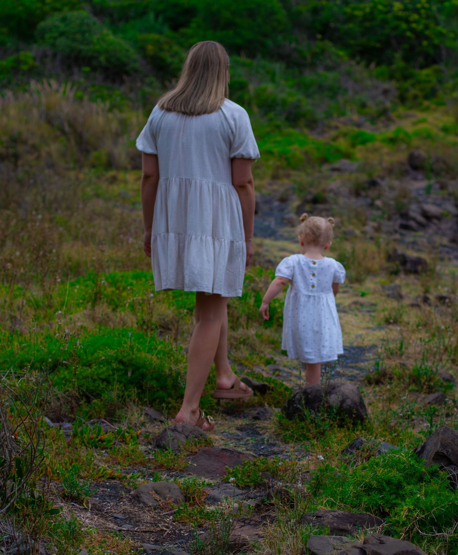 Mum walking with her young daughter as they explore a grassy coastal landscape during a relaxed family session.