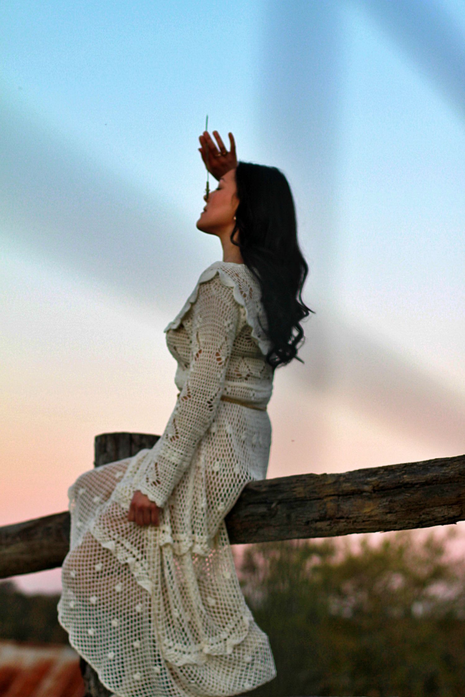Woman sitting on a fence surrounded by nature in a rural setting