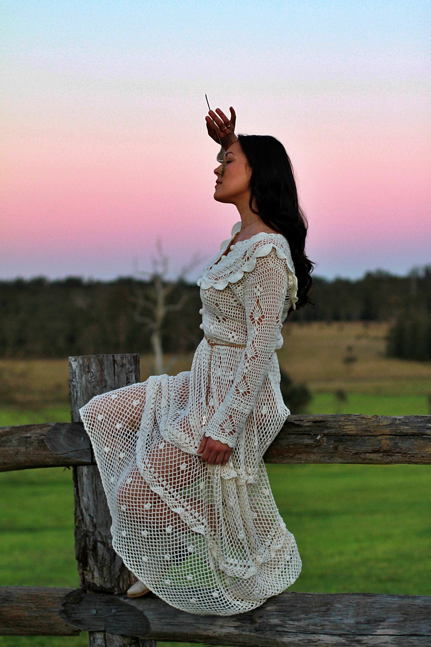 Woman sitting on a fence surrounded by nature in a rural setting