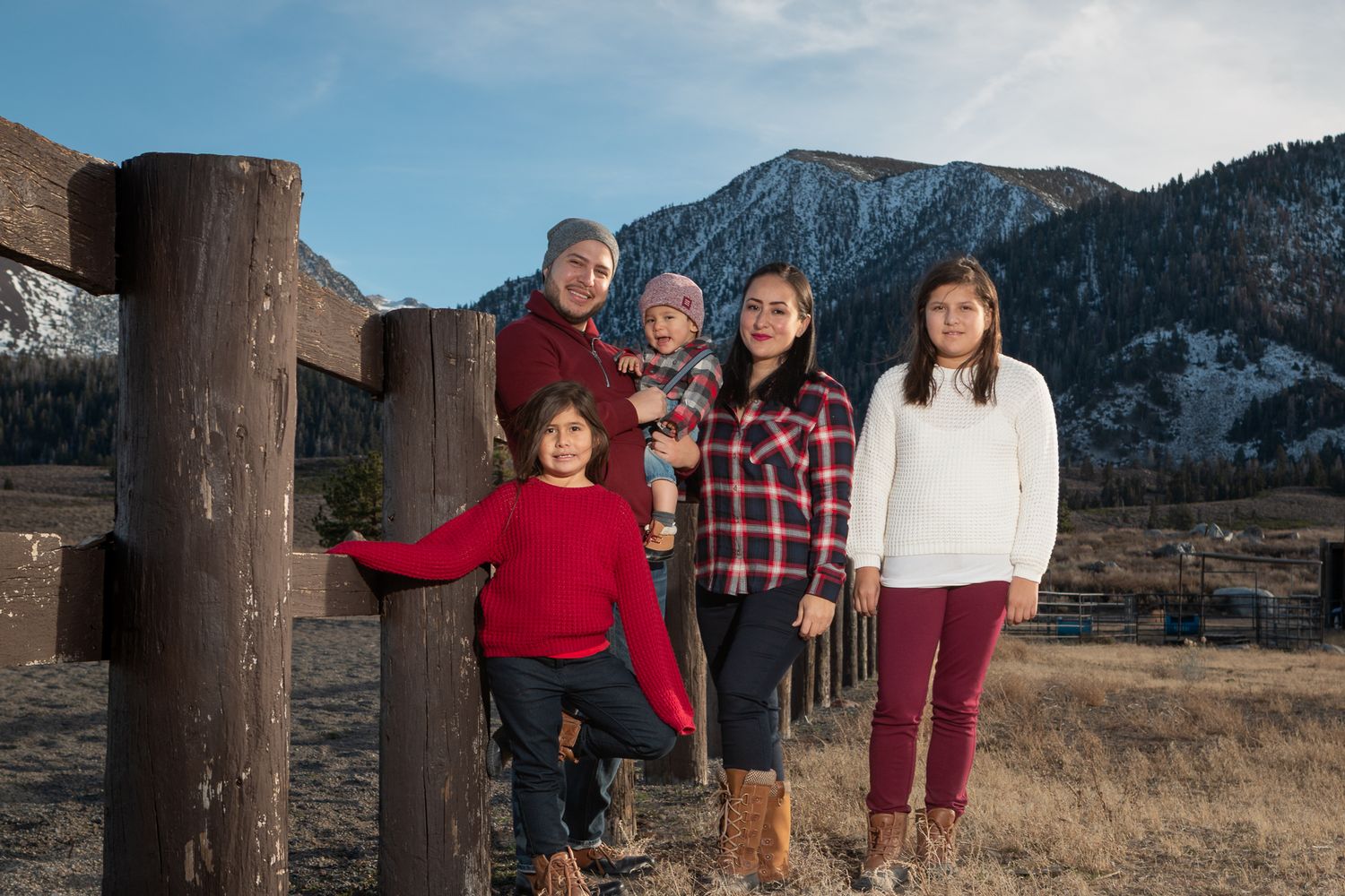A group poses by wooden fence posts with mountains and evergreen trees in the background.