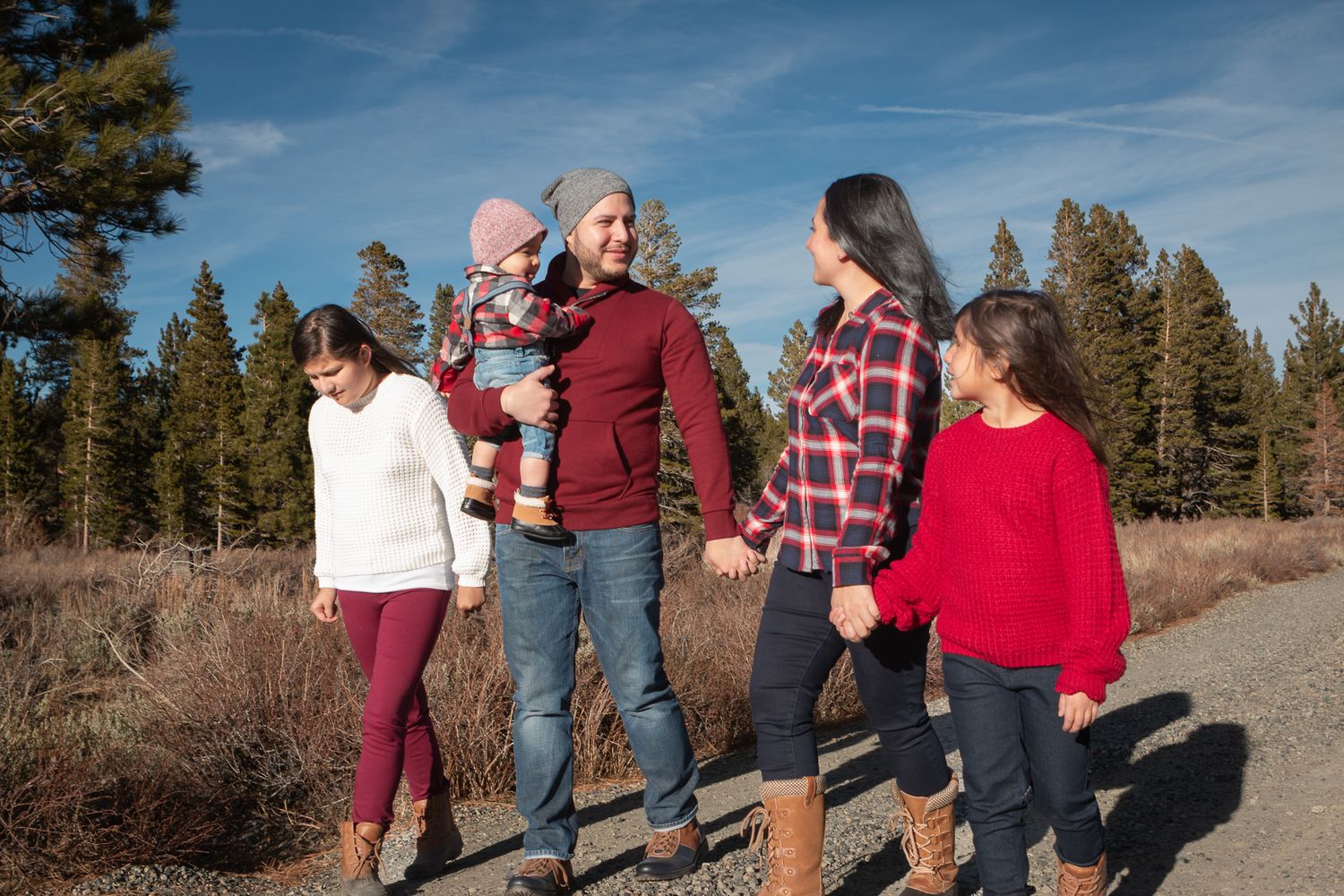 Family members walk together on a mountain path surrounded by pine trees.