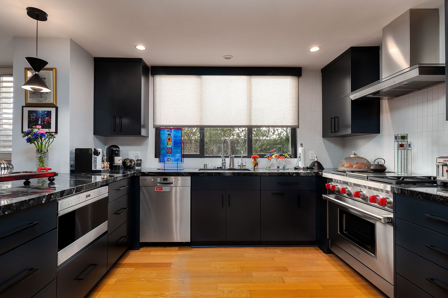 Contemporary kitchen featuring black cabinets, wood flooring, and white countertops with pendant lighting.