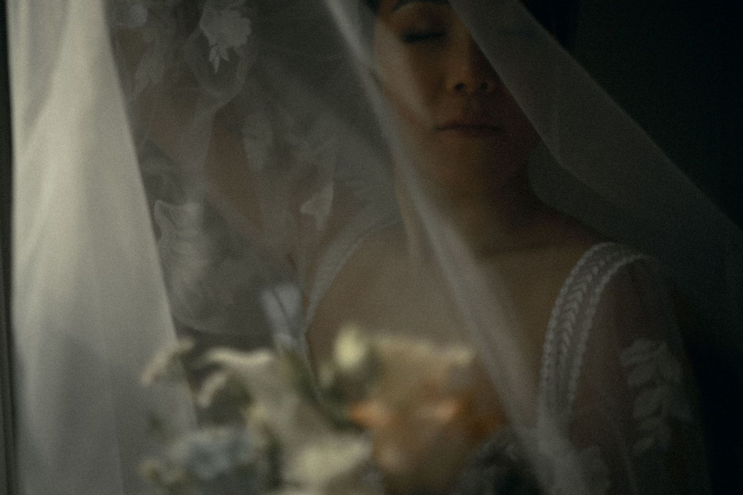 A soft and dreamy bridal portrait through a delicate veil with atmospheric smoke effects in moody lighting.