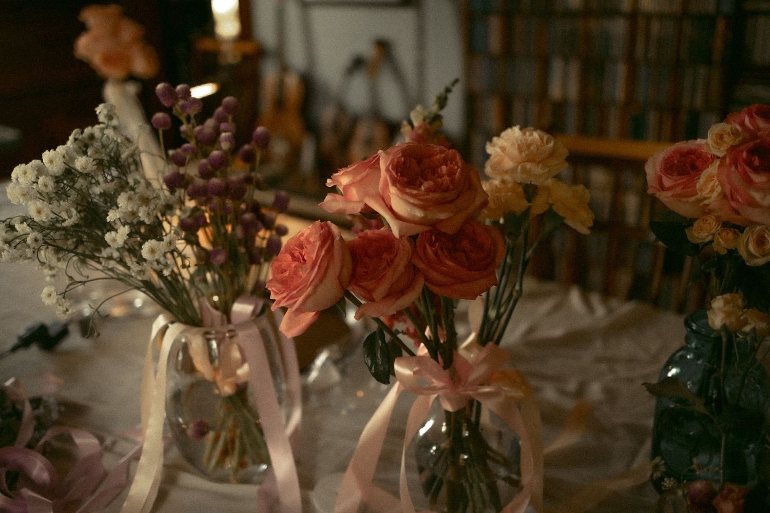 Elegant wedding centerpieces with pink roses and baby's breath in glass vases with ribbon accents.