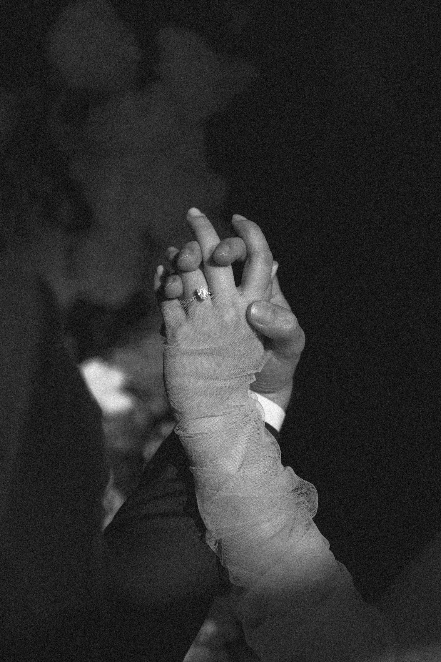 A black and white photograph of a baby's tiny hand reaching up to hold an adult's finger.