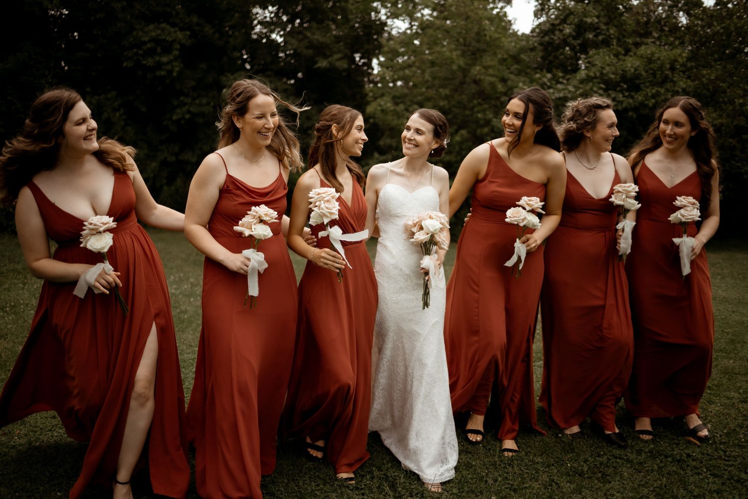 Bridesmaids in matching red dresses walking and laughing with the bride outdoors.