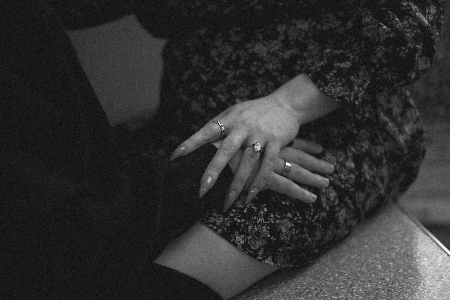 Black and white close-up photo of a hand with a ring resting on dark lace fabric.