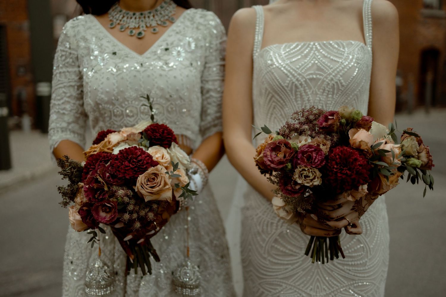 Two wedding bouquets with deep red and blush roses held against white lace dresses.