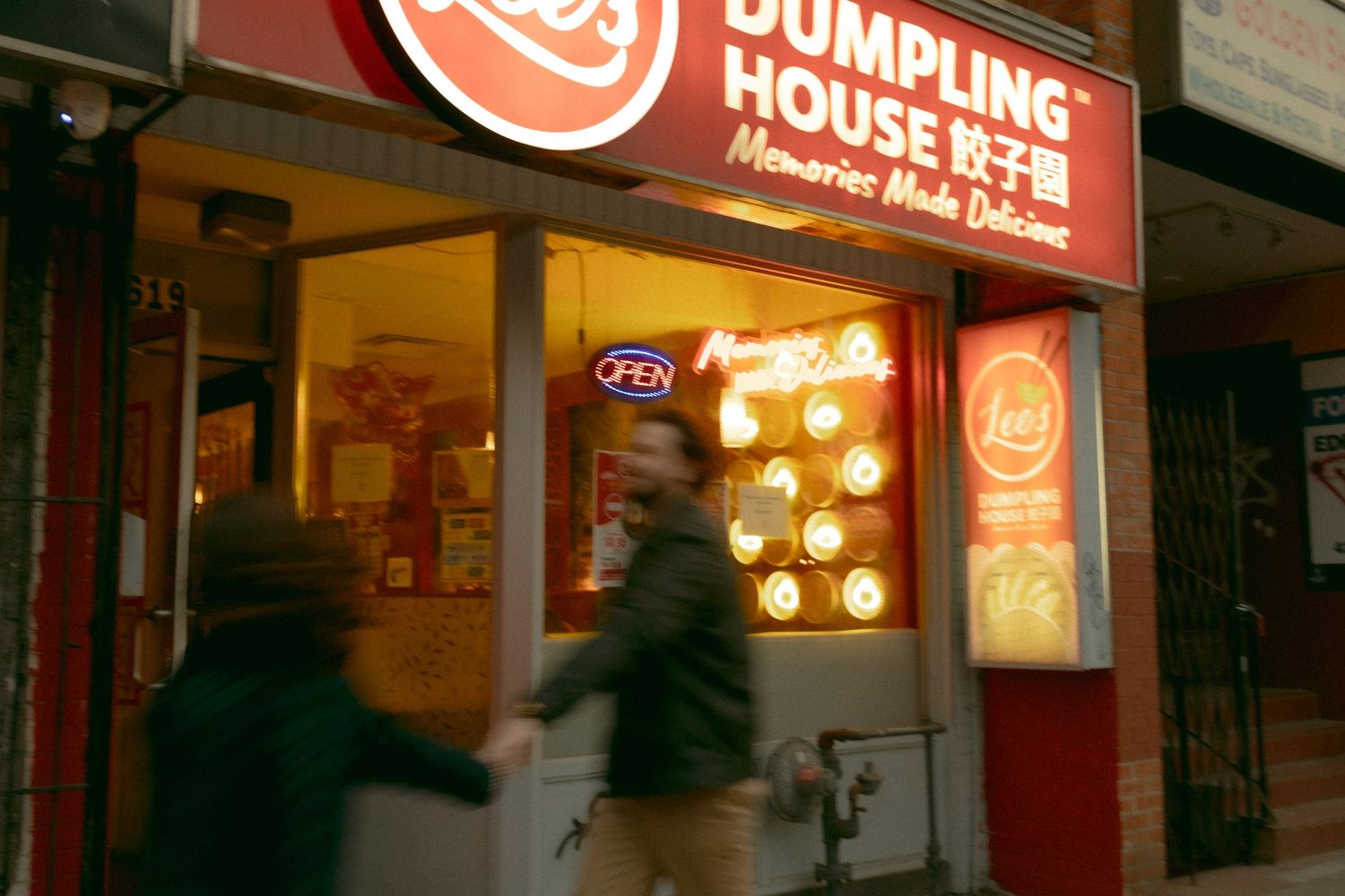 Lees Dumpling House restaurant exterior at night with neon signs and pedestrians walking by in an urban setting.