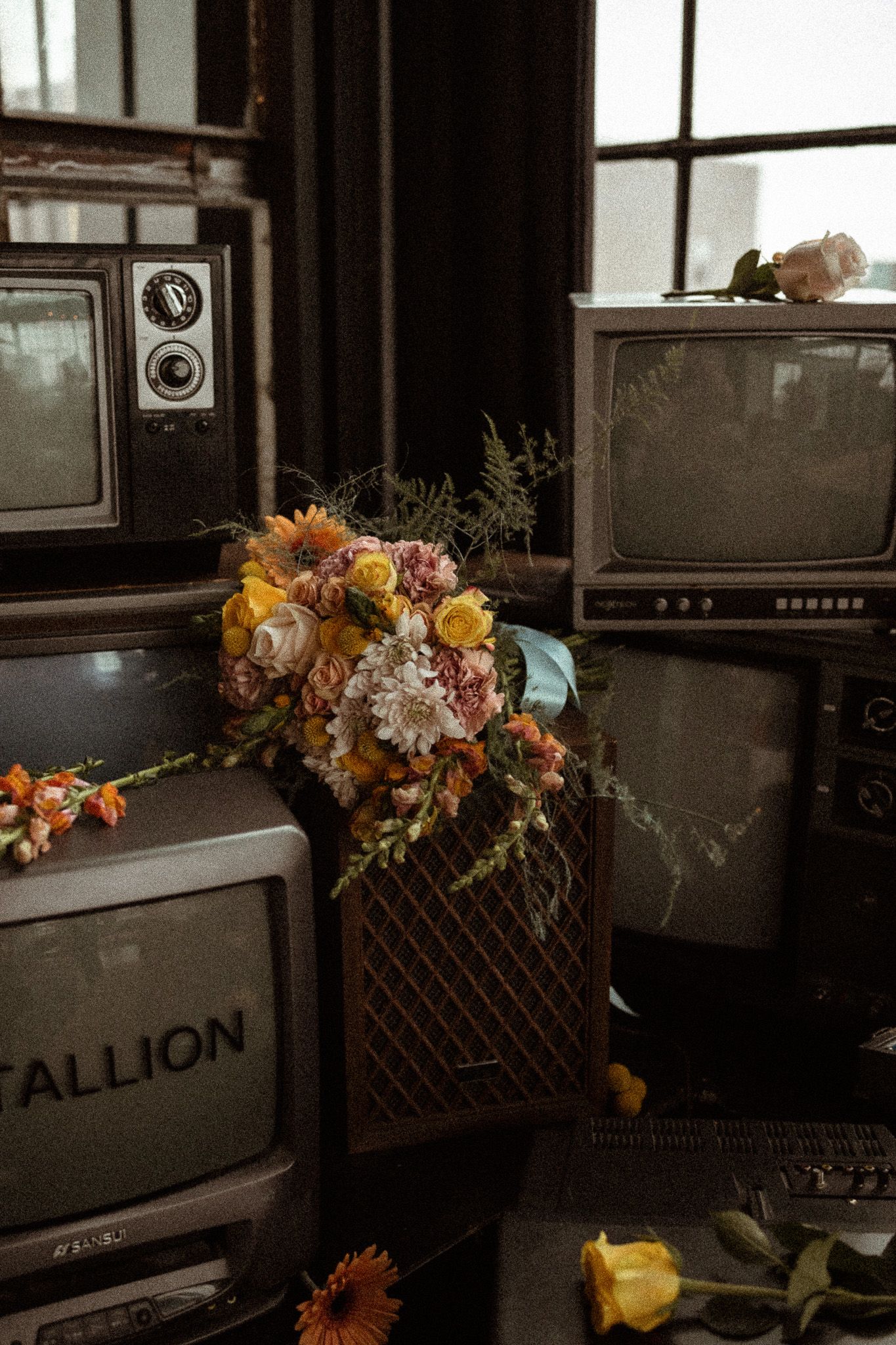 A bouquet of fall flowers arranged among vintage television sets with Stallion branding in a dark moody setting.