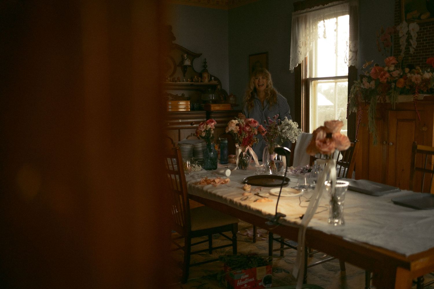 Sunlit dining room interior with flowers in vases on a rustic wooden table.