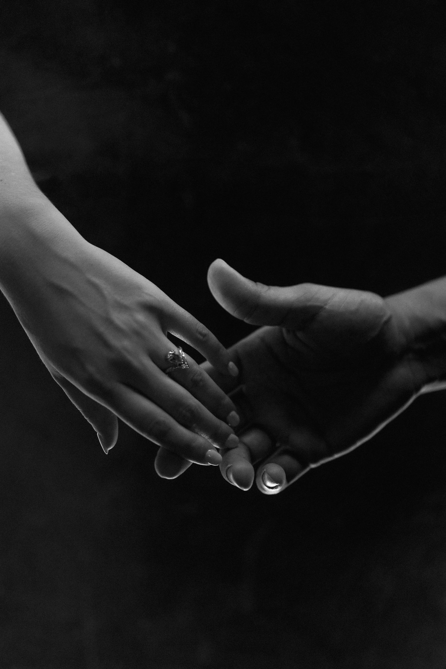 Two hands reaching towards each other tenderly with a diamond ring visible in black and white photography.