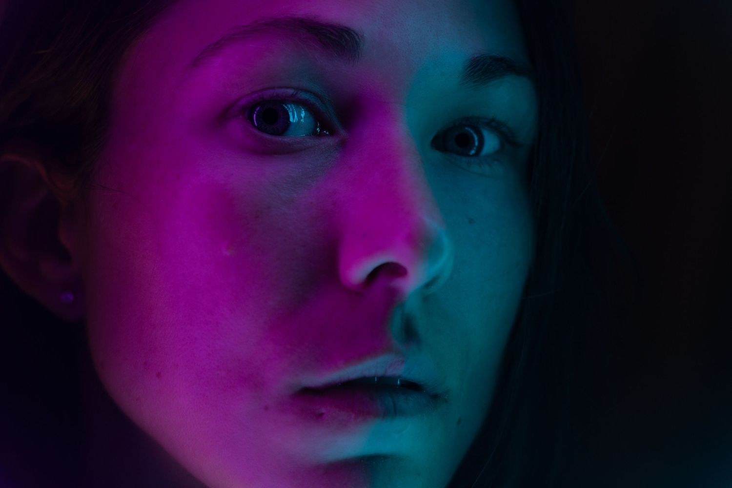 Artistic self-portrait of a female photographer illuminated by vibrant blue and purple lighting.