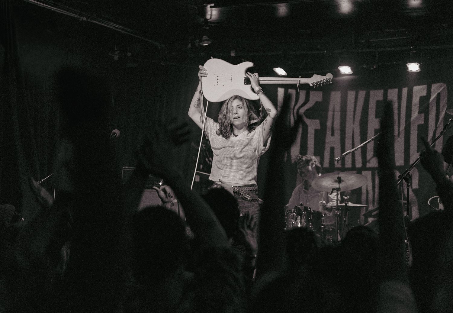 Concert photograph of a female guitarist holding her guitar above her head during a live music performance.










I prefer this respons