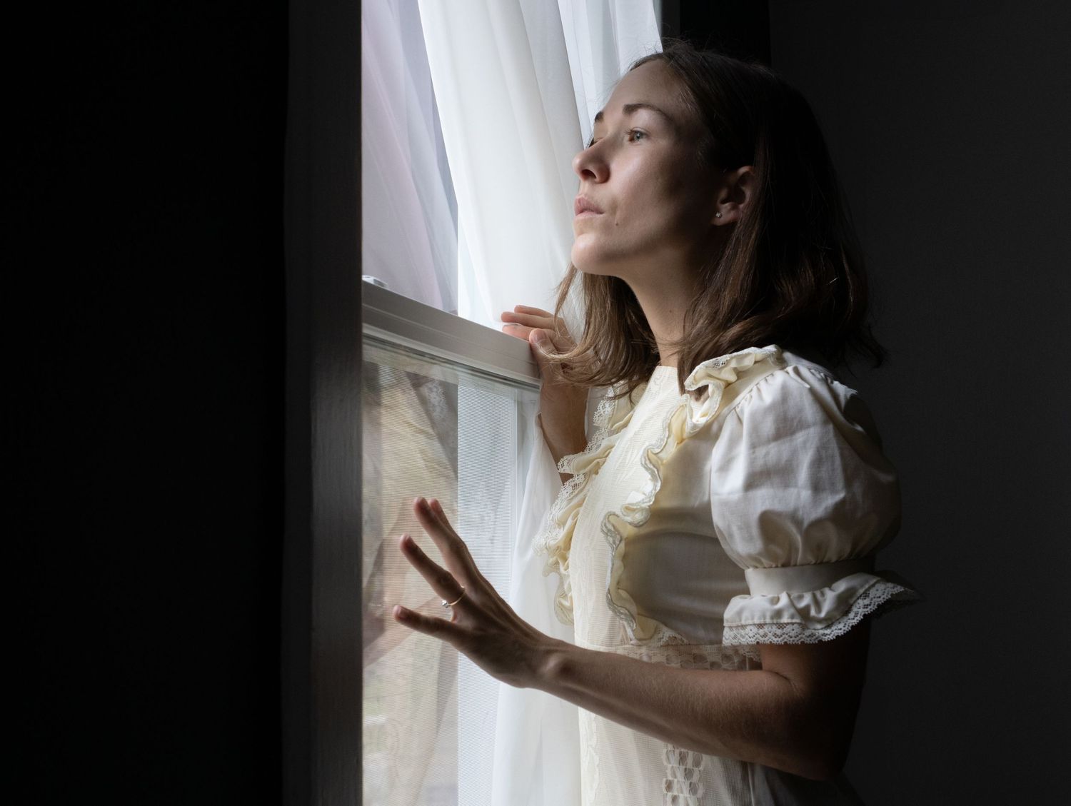 Creative self-portrait of a woman gazing out of a window in natural light.