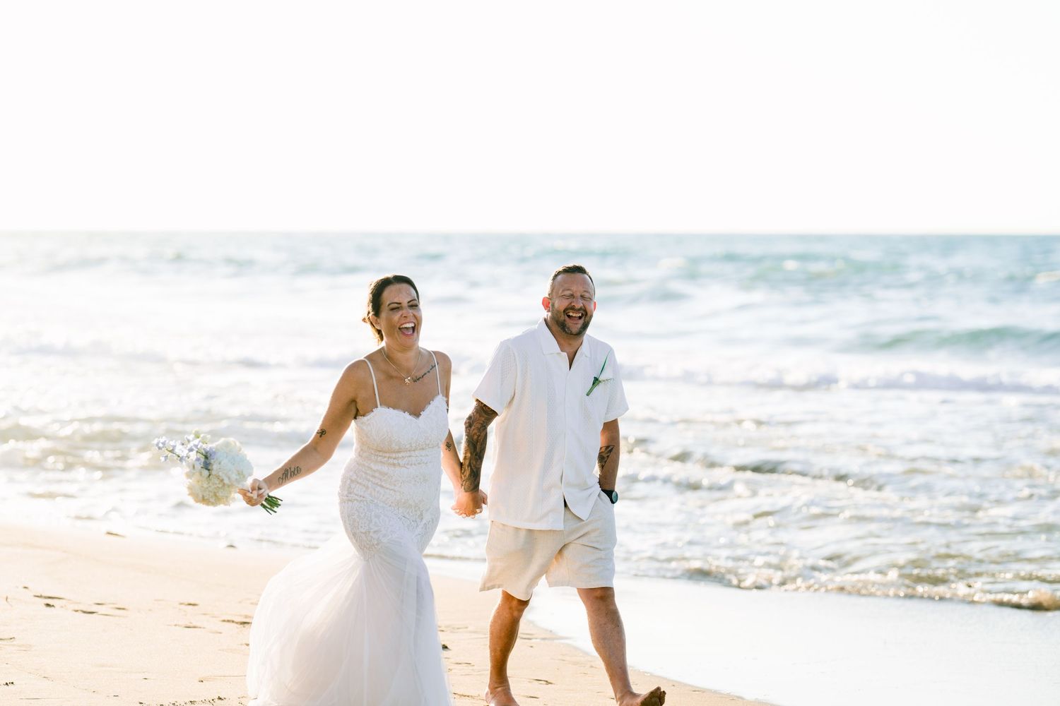 Bride and groom walking hand in hand along the shoreline, laughing, destination beach wedding in Crete