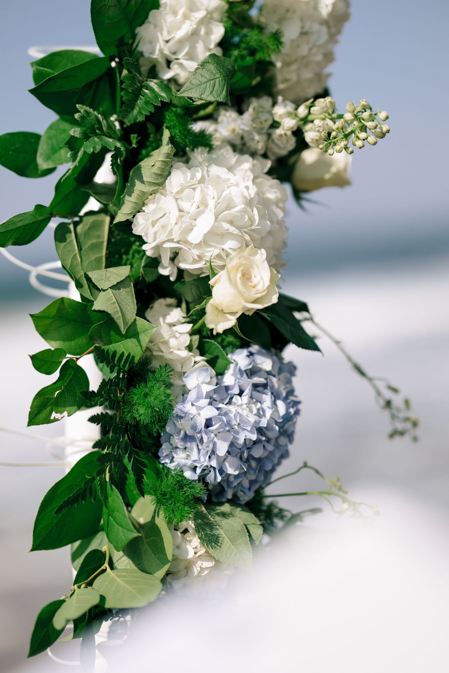 Wedding arch decorated with white hydrangeas and greenery, floral ceremony detail by the sea